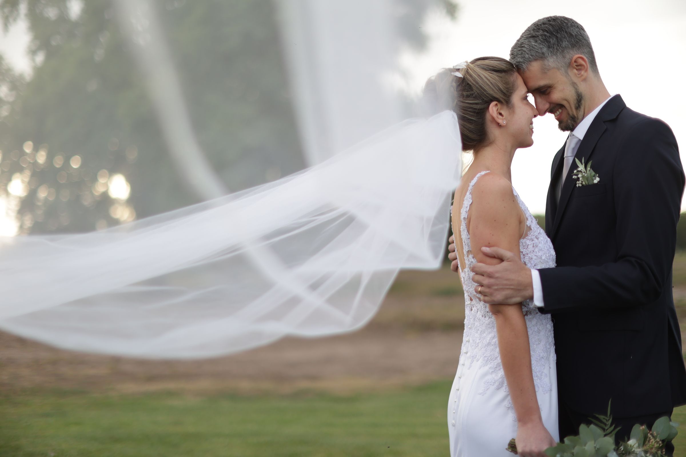 A couple sharing a quiet moment outdoors as a wedding veil floats in the evening light